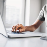 Persoon typt op een laptop aan een wit bureau