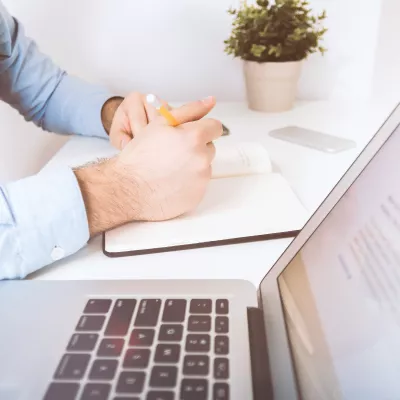 Persoon schrijft in notitieboekje naast laptop