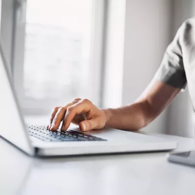 Persoon typt op een laptop aan een wit bureau