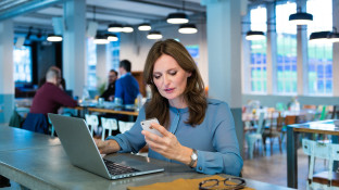 Vrouw achter laptop met telefoon in haar hand