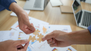 Handen houden puzzelstukjes vast boven zakelijke documenten