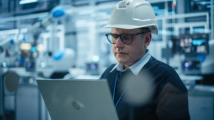 Man met helm werkt op laptop in fabriek