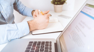Persoon schrijft in notitieboekje naast laptop