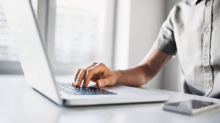 Persoon typt op een laptop aan een wit bureau