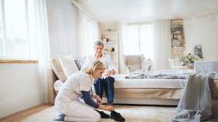Verpleger helpt oude vrouw met aantrekken schoenen